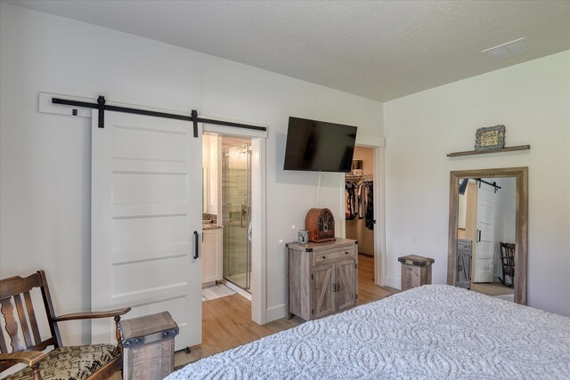 25523 N N Sheridan Rd, Chattaroy, WA 99003 - bedroom with a barn door, light wood-style flooring, a walk in closet, ensuite bathroom, and baseboards