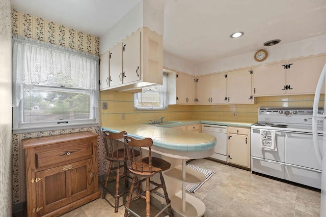 823 N Woodlawn Rd, Spokane Valley, WA 99216 - kitchen featuring white appliances, tile countertops, backsplash, a sink, and wallpapered walls