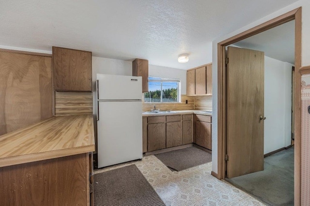 47 Davis Lake Ln, Usk, WA 99180 - kitchen with freestanding refrigerator, light countertops, a sink, a textured ceiling, and brown cabinets