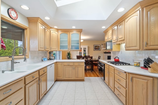 kitchen featuring stainless steel appliances, a sink, light brown cabinetry, a skylight, and light tile patterned floors