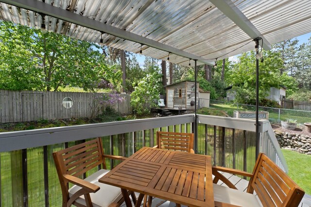 wooden deck featuring a fenced backyard, an outdoor structure, a shed, view of scattered trees, and outdoor dining area