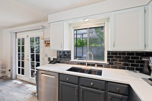 kitchen with stainless steel dishwasher, a sink, french doors, light wood finished floors, and backsplash