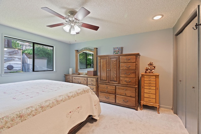 bedroom featuring a closet, light colored carpet, a textured ceiling, and ceiling fan