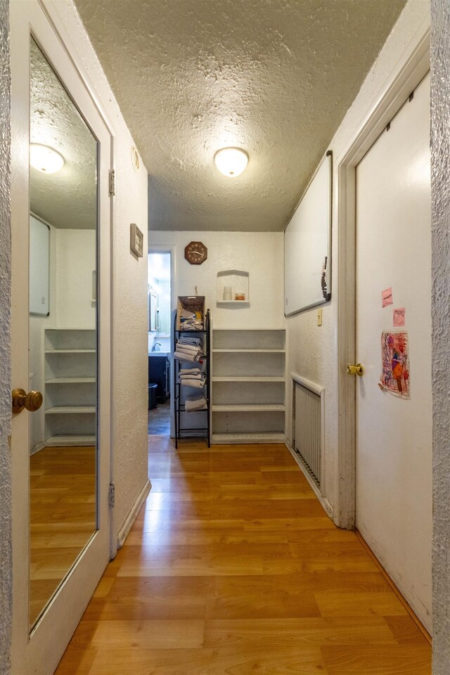 corridor with a textured ceiling and light wood finished floors