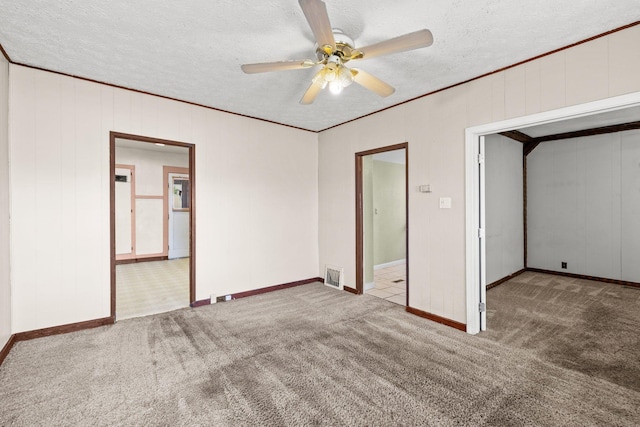 unfurnished room featuring carpet flooring, a textured ceiling, a ceiling fan, baseboards, and ornamental molding
