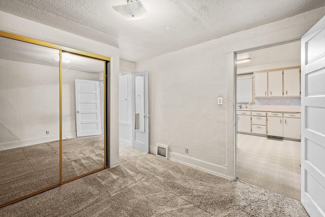 unfurnished bedroom with light colored carpet, a textured ceiling, a closet, a textured wall, and baseboards