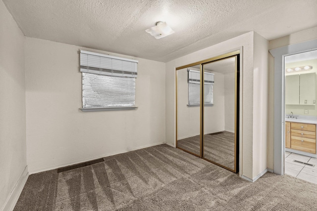unfurnished bedroom with carpet flooring, a closet, a textured ceiling, a sink, and ensuite bath