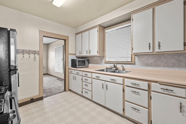 kitchen with a sink, stainless steel microwave, light countertops, stove, and light floors