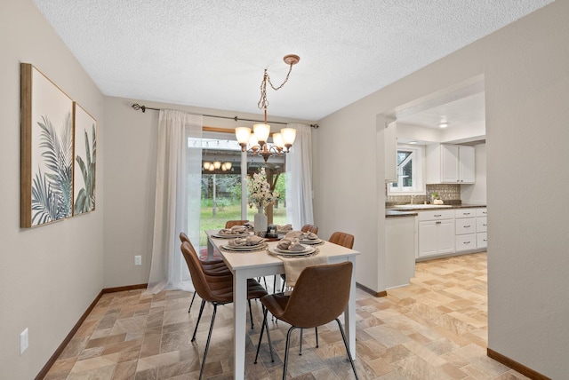 dining area featuring a chandelier, stone finish floors, baseboards, and a textured ceiling