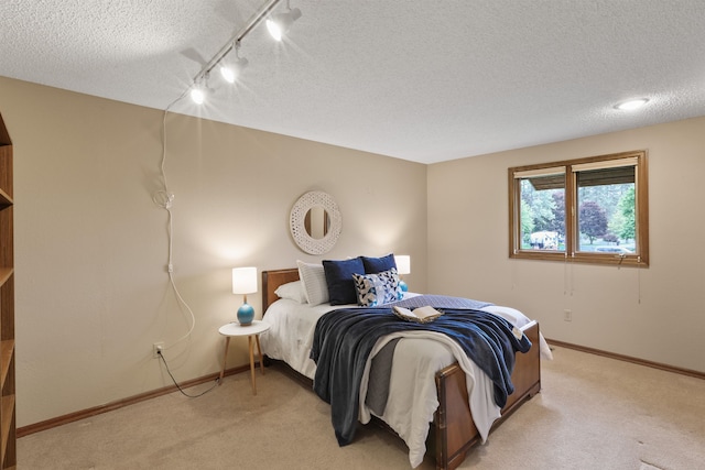 bedroom featuring a textured ceiling, light colored carpet, rail lighting, and baseboards