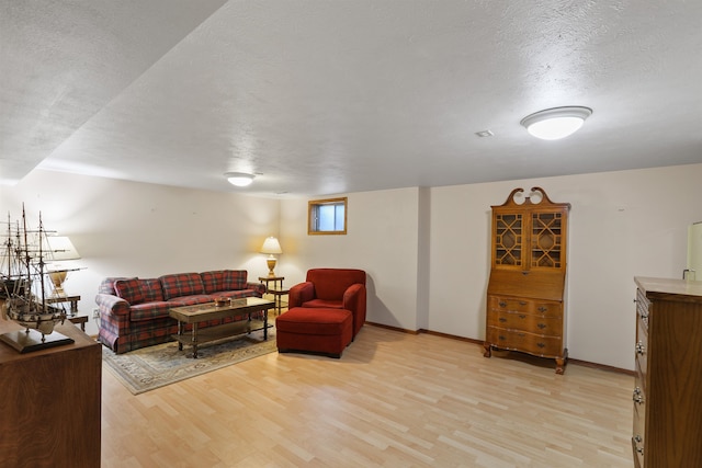 living area featuring light wood-style flooring, a textured ceiling, and baseboards
