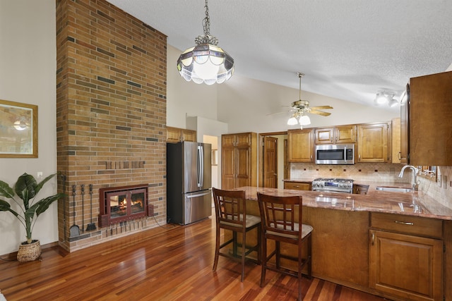 kitchen featuring appliances with stainless steel finishes, a sink, a peninsula, a textured ceiling, and decorative backsplash