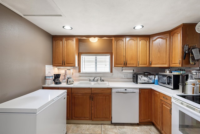 kitchen with white appliances, a sink, tasteful backsplash, brown cabinetry, and recessed lighting