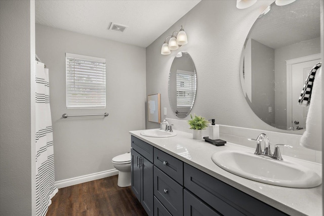 bathroom featuring wood finished floors, double vanity, toilet, and baseboards