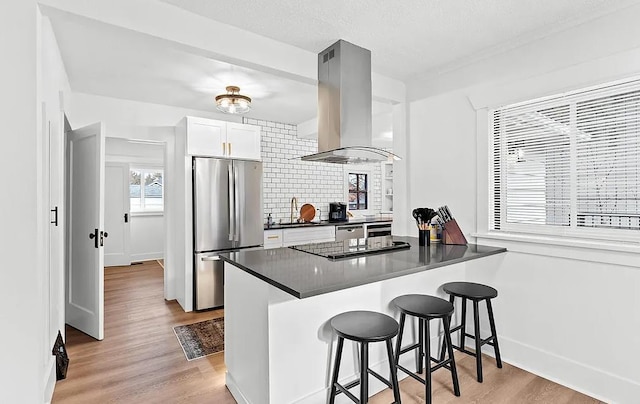 kitchen featuring freestanding refrigerator, island exhaust hood, black electric stovetop, dark countertops, and light wood-type flooring