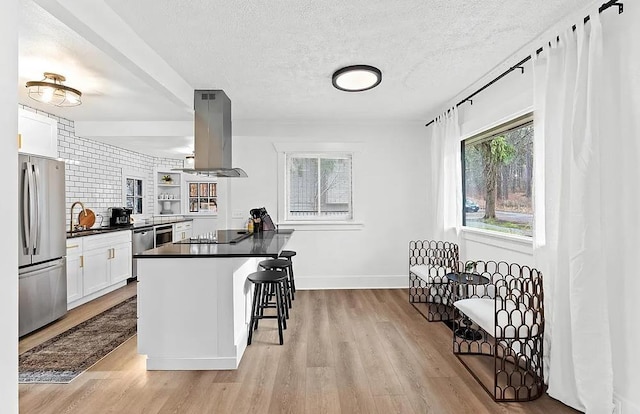 kitchen featuring stainless steel appliances, island exhaust hood, dark countertops, a kitchen breakfast bar, and healthy amount of natural light