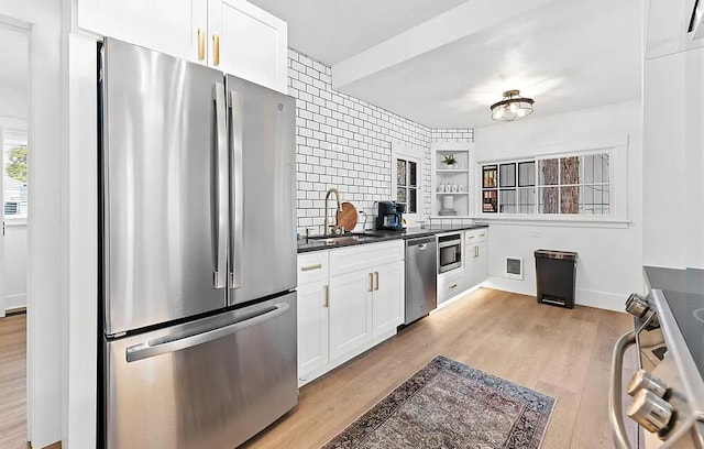 kitchen featuring appliances with stainless steel finishes, a sink, dark countertops, open shelves, and light wood-type flooring