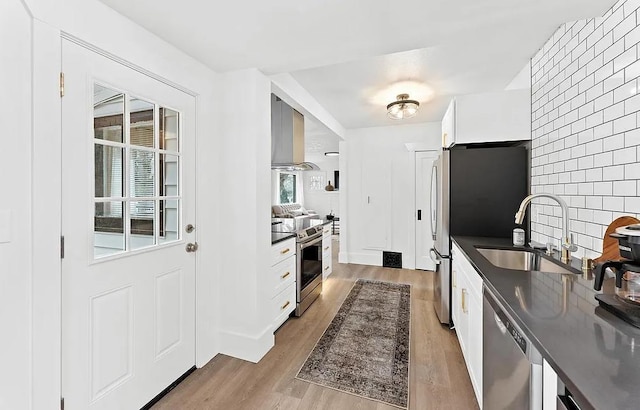 kitchen with stainless steel appliances, a sink, dark countertops, light wood-style flooring, and decorative backsplash