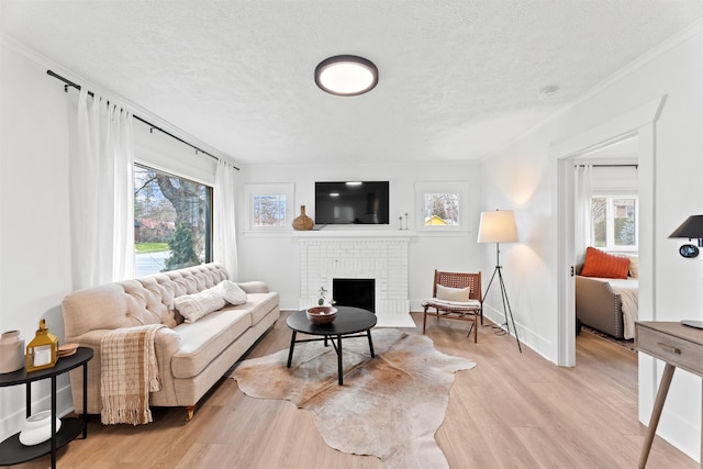 living room with plenty of natural light, a textured ceiling, light wood-style flooring, a brick fireplace, and crown molding