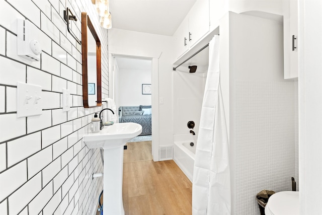 bathroom with tile walls, wood finished floors, toilet, connected bathroom, and shower / bathtub combination with curtain