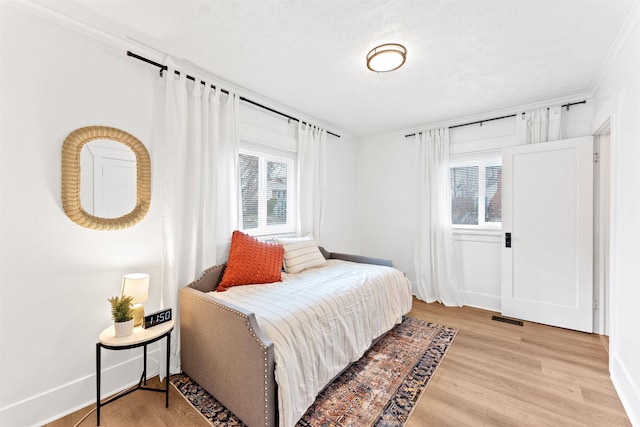 bedroom with baseboards, light wood finished floors, and crown molding