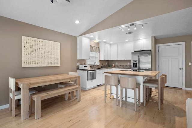 kitchen with appliances with stainless steel finishes, white cabinets, vaulted ceiling, light wood-style floors, and a breakfast bar area