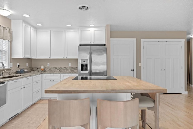 kitchen featuring stainless steel fridge, butcher block countertops, a sink, black electric cooktop, and white cabinets