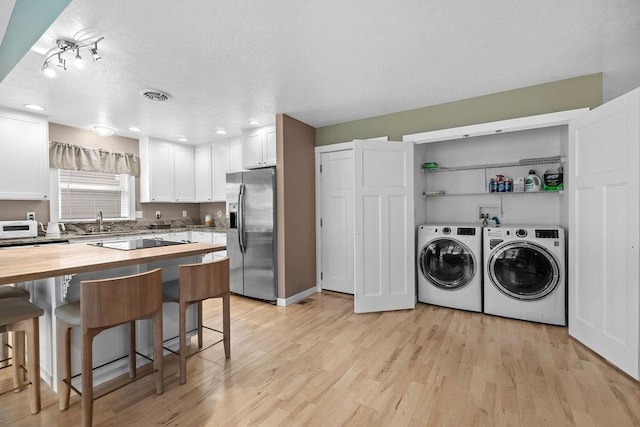 kitchen with stainless steel refrigerator with ice dispenser, wood counters, a breakfast bar area, washer and clothes dryer, and white cabinetry