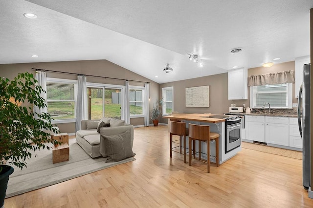 kitchen featuring stainless steel appliances, open floor plan, white cabinets, a kitchen breakfast bar, and light wood-style floors