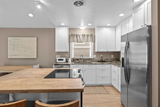 kitchen featuring stainless steel fridge with ice dispenser, a sink, white cabinets, wood counters, and recessed lighting