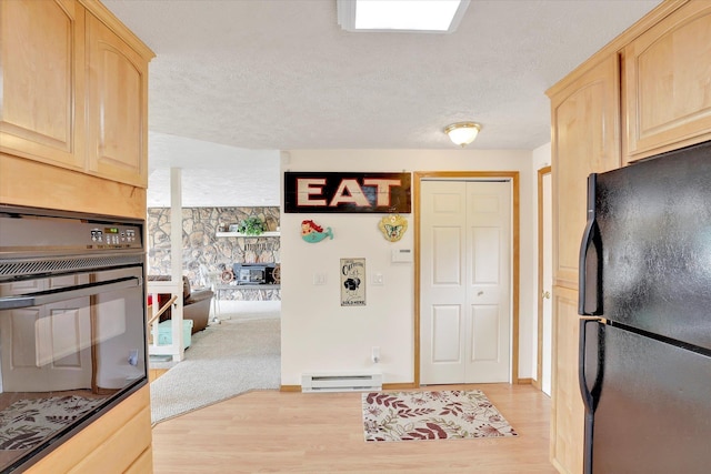 13227 N E Newman Lake Dr, Newman Lake, WA 99025 - kitchen featuring black appliances, light brown cabinets, a baseboard radiator, a wood stove, and light wood finished floors