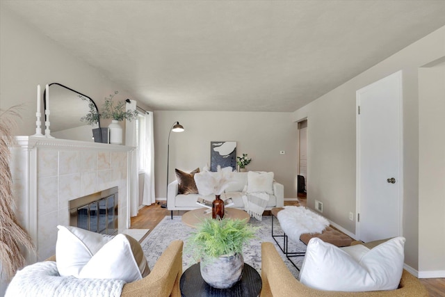 living area featuring a tile fireplace, baseboards, and wood finished floors