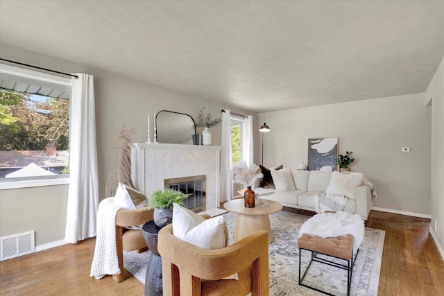 living room featuring baseboards, wood finished floors, a tiled fireplace, and plenty of natural light