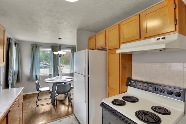 kitchen with white appliances, under cabinet range hood, a chandelier, wood finished floors, and light countertops