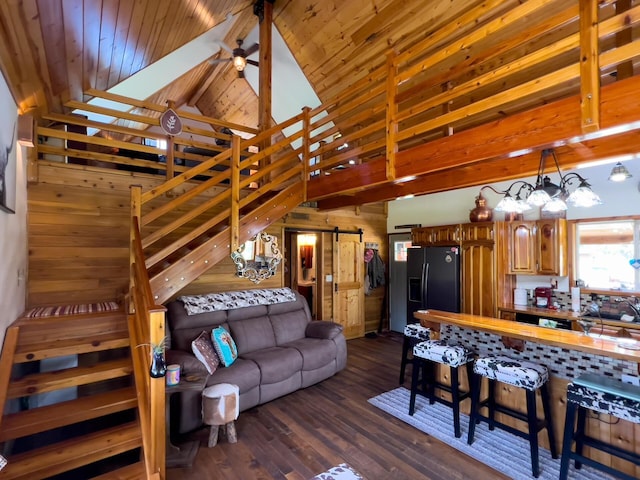 living area featuring a barn door, dark wood-style flooring, beam ceiling, stairway, and wooden walls