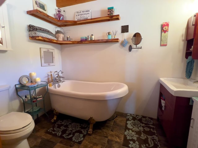 full bathroom featuring toilet, vanity, a freestanding tub, and stone finish floors