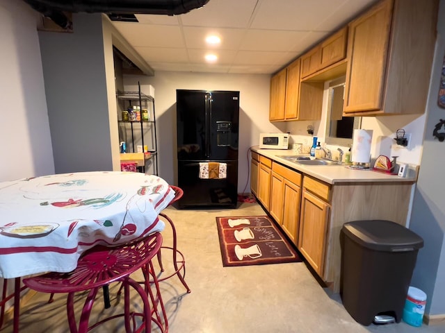 kitchen with black fridge with ice dispenser, a sink, white microwave, a drop ceiling, and light countertops