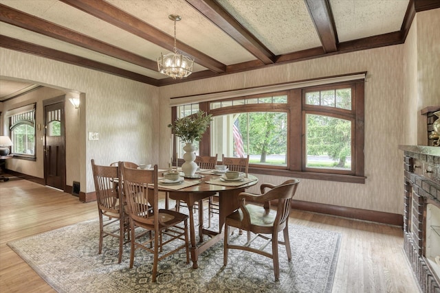 dining room featuring wood finished floors, baseboards, a fireplace, beamed ceiling, and wallpapered walls