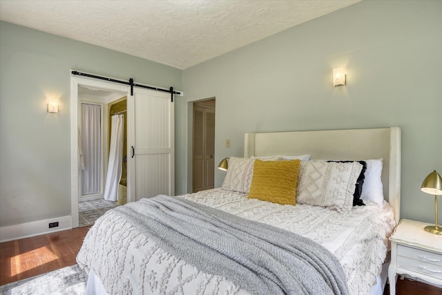 bedroom with a barn door, wood finished floors, baseboards, and a textured ceiling