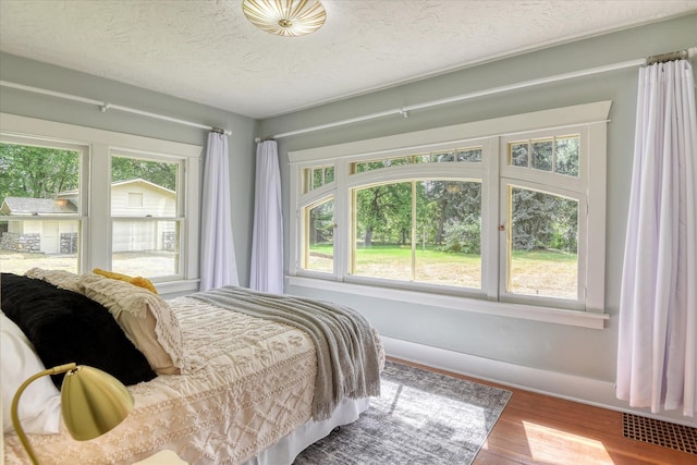 bedroom with wood finished floors, baseboards, and a textured ceiling