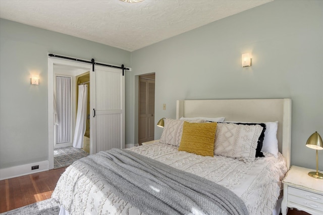 bedroom with wood finished floors, a barn door, baseboards, a textured ceiling, and a closet