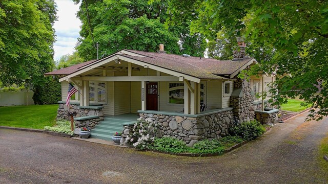 10228 N Whitworth Dr, Spokane, WA 99218 - view of front of home with stone siding, covered porch, a shingled roof, and a front lawn