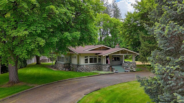 10228 N Whitworth Dr, Spokane, WA 99218 - view of front of house with stone siding, a porch, a front lawn, a chimney, and asphalt driveway