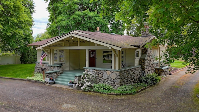 view of front facade featuring stone siding, a porch, a shingled roof, and a front lawn