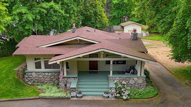 10228 N Whitworth Dr, Spokane, WA 99218 - view of front facade with a shingled roof, stone siding, a chimney, a porch, and a front lawn