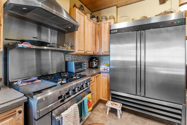 kitchen featuring built in fridge, wall chimney exhaust hood, backsplash, dark countertops, and light brown cabinetry