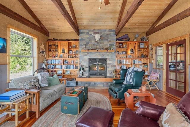living area featuring wood finished floors, wooden ceiling, a stone fireplace, and a ceiling fan