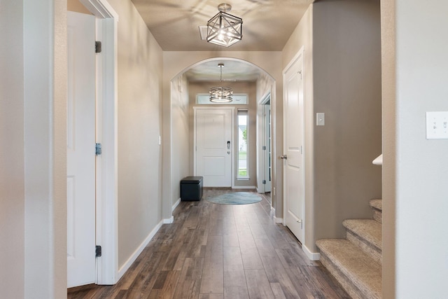 foyer entrance featuring arched walkways, a chandelier, baseboards, and dark wood finished floors