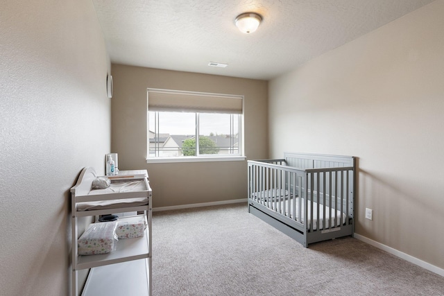 carpeted bedroom featuring baseboards, a nursery area, and a textured ceiling