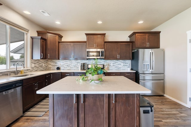 kitchen featuring stainless steel appliances, a sink, wood finished floors, decorative backsplash, and a center island